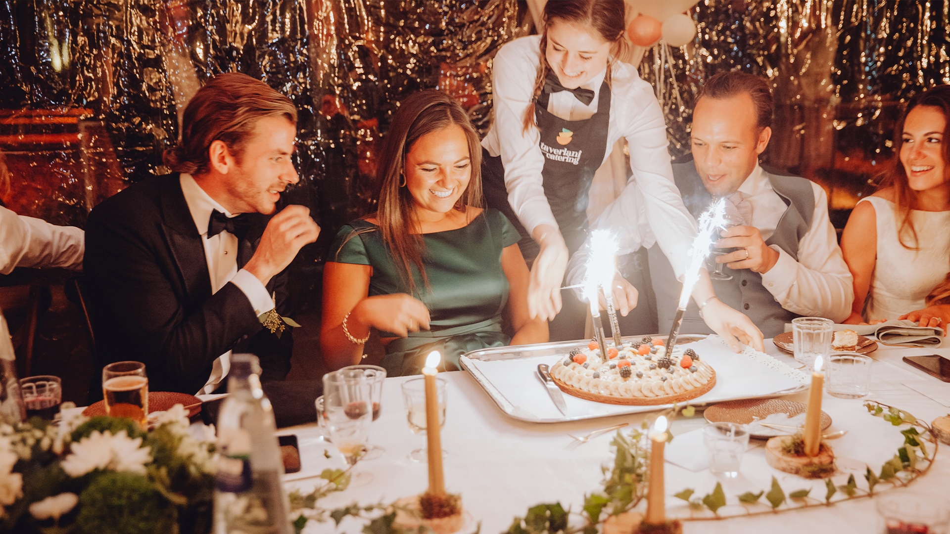 Serveerster met Taverlani-schort reikt een taart met sterretjes aan tussen lachende gasten